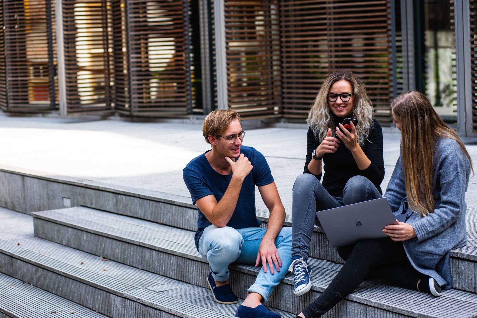 Tři studenti s notebookem na venkovních schodech